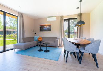Moderne woonkamer in Vakantievilla Amalia 6 met zetel, eethoek en grote ramen in Hofparken De Bergvennen, Nederland.