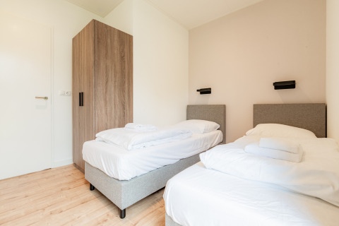 Modernes Schlafzimmer mit zwei Einzelbetten, weißer Bettwäsche und Holzschrank in Vakantievilla Amalia 6.
