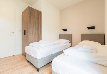 Chambre moderne à deux lits simples, linge blanc et armoire boisée à la Vakantievilla Amalia 6, Pays-Bas.
