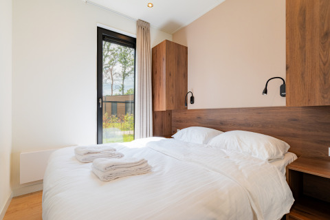 Camera luminosa con letto matrimoniale, dettagli in legno, grande finestra e asciugamani in una villa vacanza.