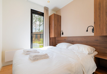 Lichte slaapkamer met tweepersoonsbed, houten elementen, groot raam en handdoeken in een vakantievilla.