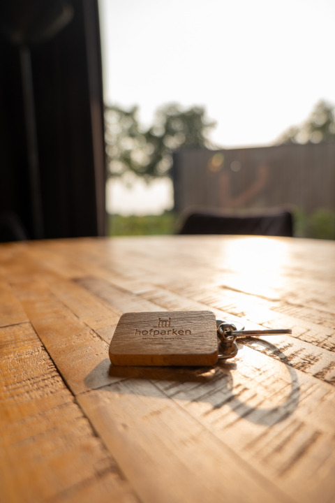 Clé avec porte-clé Hofparken De Bergvennen sur table en bois à Vakantievilla Amalia 6 au coucher du soleil.