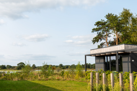 Moderne lodge med store vinduer ved Hofparken De Bergvennen, omkranset af grøn natur og træer.