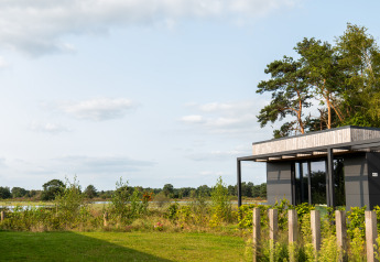 Moderne lodge met grote ramen bij Hofparken De Bergvennen, Nederland, omgeven door groen en bomen.