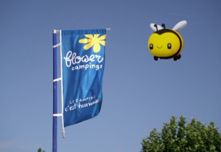 Flower Campings Flagge und große Bienen-Drachenfigur fliegen über Baumwipfeln in einem französischen Ferienpark.