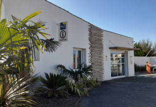 Edificio della reception di Flower Camping Le Pré des Sables in Pays de la Loire, Francia, con palme vicine.