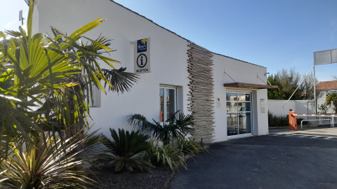 Reception building at Flower Camping Le Pré des Sables in Pays de la Loire, France, with palm trees nearby.