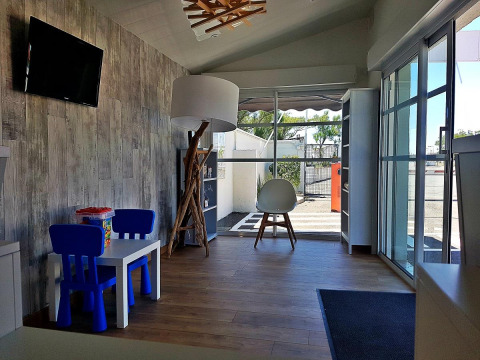 Heller Aufenthaltsraum mit Kinderbereich und großen Fenstern im Flower Camping Le Pré des Sables, Frankreich.