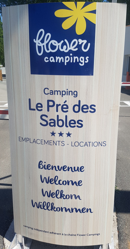 Cartello di Flower Camping Le Pré des Sables in Pays de la Loire, Francia, con benvenuto multilingue.