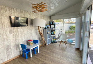 Sala de espera moderna e iluminada con mesa infantil, sillas azules, exhibidor de folletos y ventanal grande.