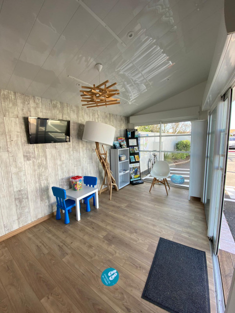 Bright, modern indoor waiting area with kids' table, blue chairs, info stand, and large window view.