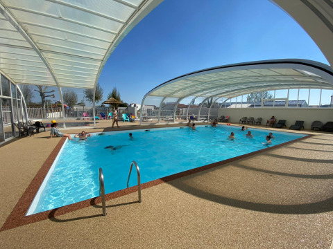 Überdachtes Schwimmbad im Ferienpark mit Gästen, die entspannen und schwimmen, sonniger Tag draußen.
