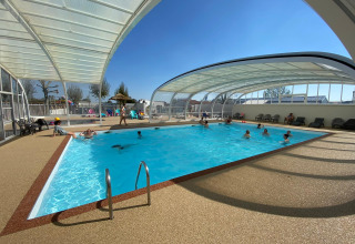 Piscina cubierta en parque vacacional con personas nadando y descansando, ambiente soleado y relajado.