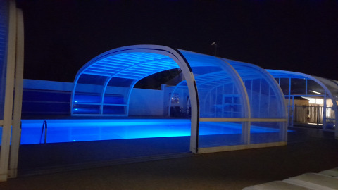 Oplyst overdækket swimmingpool om natten på Flower Camping Le Pré des Sables i Pays de la Loire, Frankrig.