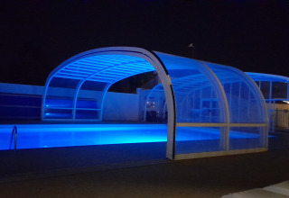 Illuminated covered swimming pool at night at Flower Camping Le Pré des Sables in Pays de la Loire, France.