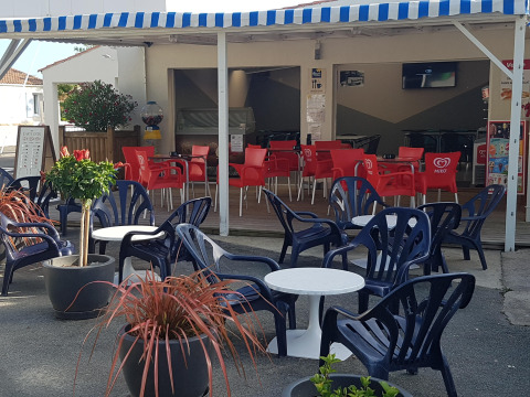 Terrasse de café avec chaises bleues et tables blanches au Flower Camping Le Pré des Sables, Pays de la Loire.