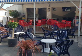 Außensitzbereich eines Cafés mit blauen Plastikstühlen und weißen Tischen im Flower Camping Le Pré des Sables.