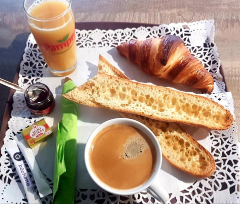 Colazione francese con croissant, baguette, caffè, succo d’arancia, burro e marmellata su un vassoio.