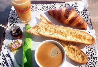 Colazione francese con croissant, baguette, caffè, succo d’arancia, burro e marmellata su un vassoio.