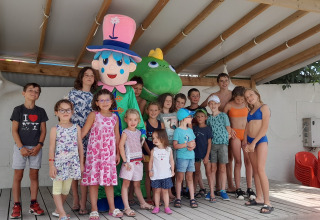 Eine Gruppe Kinder und Erwachsene posiert mit zwei Maskottchen unter einem überdachten Bereich im Ferienpark.