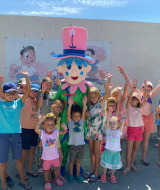 Children gather around a cheerful mascot at Flower Camping Le Pré des Sables in Pays de la Loire, France.