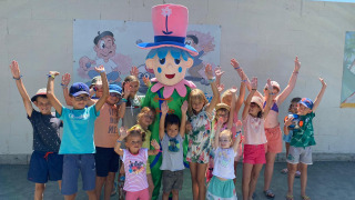 Children gather around a cheerful mascot at Flower Camping Le Pré des Sables in Pays de la Loire, France.