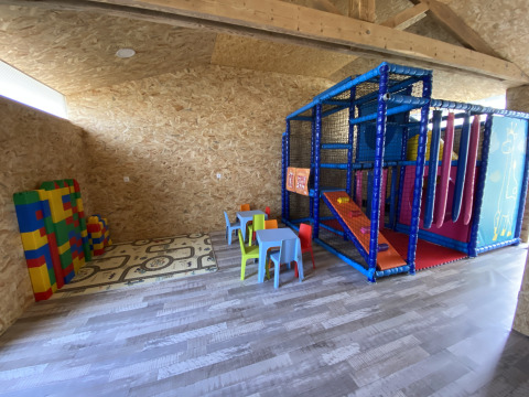 Indoor-Spielzimmer im Flower Camping Le Pré des Sables mit Bauklötzen, Kindertischen und Klettergerüst.