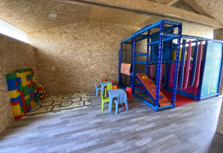 Salle de jeux intérieure au Flower Camping Le Pré des Sables avec grands blocs, tables et aire de jeux.