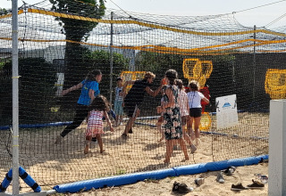 Children play in a sand-filled, netted area at Flower Camping Le Pré des Sables in Pays de la Loire, France.