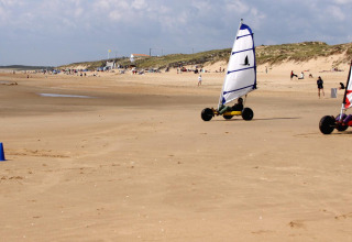 Two land sailboats with colorful sails race along the wide sandy beach at Flower Camping Le Pré des Sables, France.