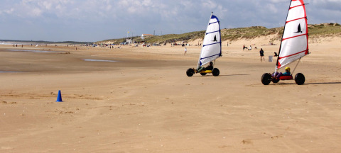 Zwei Strandsegler mit bunten Segeln fahren am breiten Sandstrand bei Flower Camping Le Pré des Sables, Frankreich.