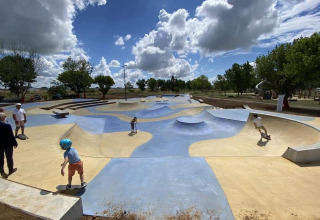 Børneskatepark med farvede ramper og flere børn, under en skyet himmel i en park i Frankrig.
