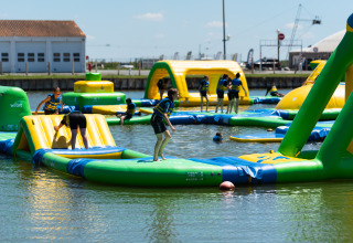 Personen spielen im großen aufblasbaren Wasserpark bei Flower Camping Le Pré des Sables in Pays de la Loire, Frankreich.