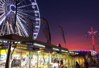 Abendaufnahme eines Vergnügungsparks mit Riesenrad und bunten Lichtern im Flower Camping Le Pré des Sables.