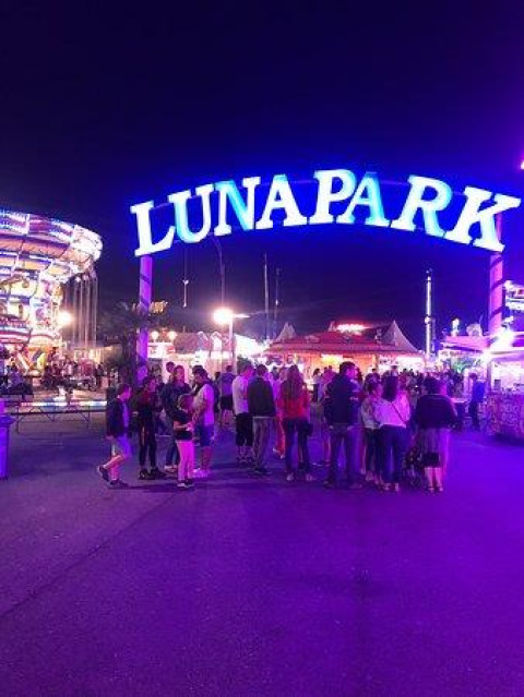 Enseigne lumineuse LUNAPARK à l'entrée d'un parc d'attractions la nuit avec des gens rassemblés.
