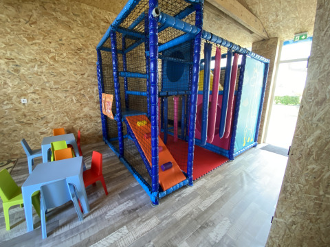 Binnen speelruimte met kleurrijke klimconstructie, glijbaan en kleine tafeltjes en stoelen voor kinderen.