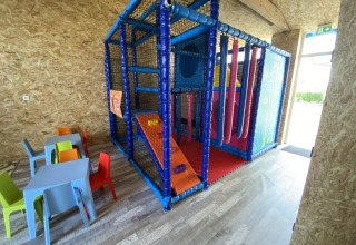 Overdekte speeltuin met kleurrijke klimstructuur, kleine tafels en stoelen voor kinderen in een lichte ruimte.