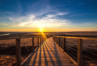 Vista de la puesta de sol desde una pasarela de madera en la playa de Flower Camping Le Pré des Sables, Pays de la Loire, Francia.