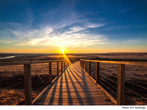 Vista de la puesta de sol desde una pasarela de madera en la playa de Flower Camping Le Pré des Sables, Pays de la Loire, Francia.