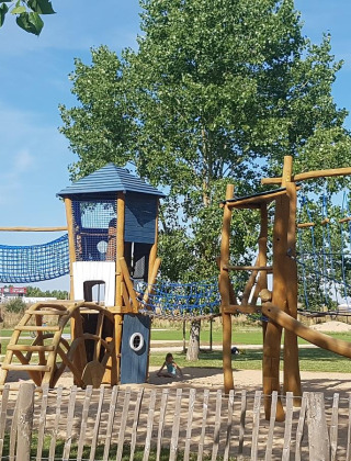 Playground with towers, climbing nets, and wooden structures at Flower Camping Le Pré des Sables, France.
