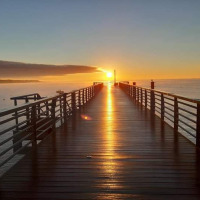 Beautiful sunrise over a pier in L'Aiguillon sur Mer, Pays de la Loire, France, with the sun reflecting on the water.