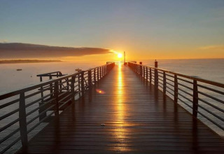 Beautiful sunrise over a pier in L'Aiguillon sur Mer, Pays de la Loire, France, with the sun reflecting on the water.