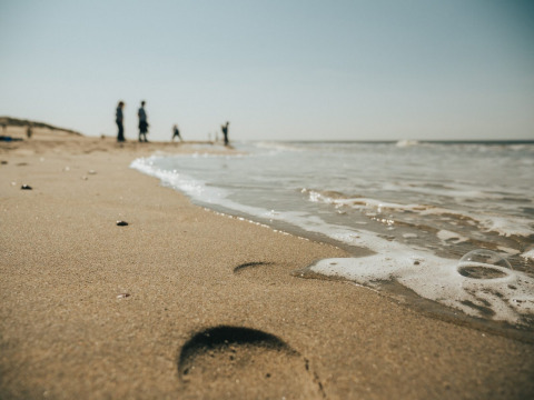 Zandstrand met voetafdruk en branding, mensen op de achtergrond bij Ouddorp in Zuid-Holland, Nederland.