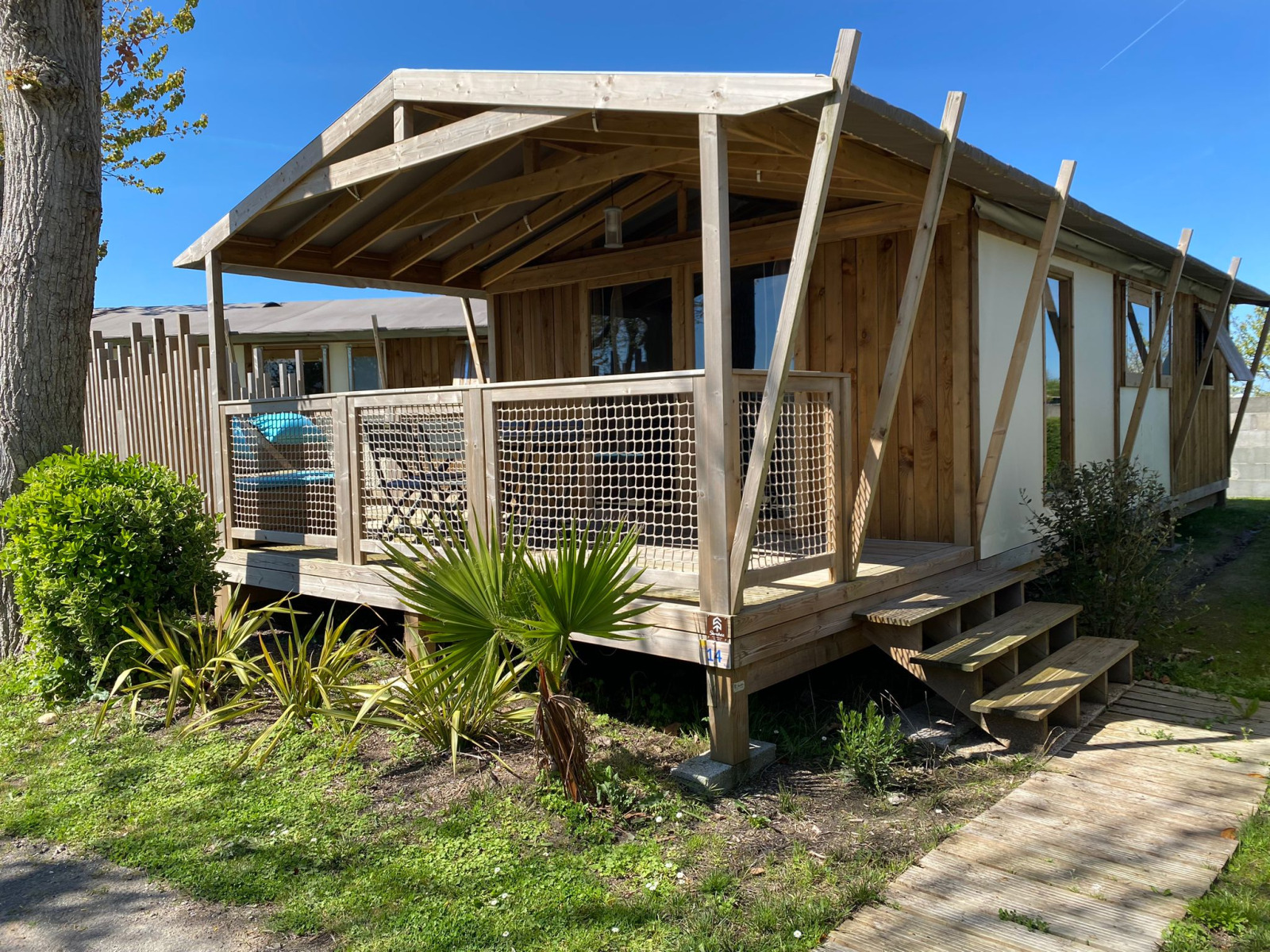 Cabane lodge Sweet Flower Premium: houten chalet met overdekte veranda en tuin op een zonnige dag.