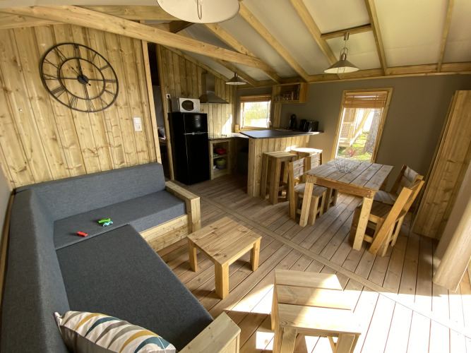 Innenansicht der Cabane lodge Sweet Flower Premium mit Holzmöbeln, Sofa und Küche auf dem Campingplatz.