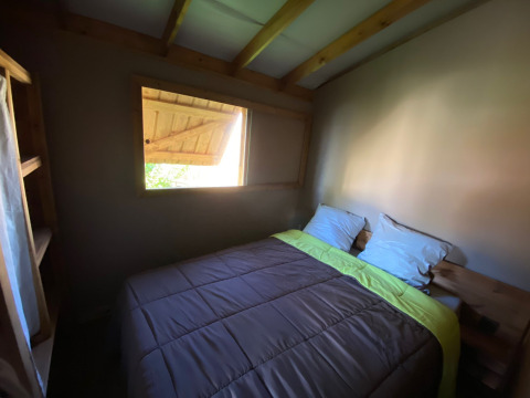 Knusse slaapkamer met tweepersoonsbed, houten plafond en raam in Cabane lodge Sweet Flower Premium, Frankrijk.