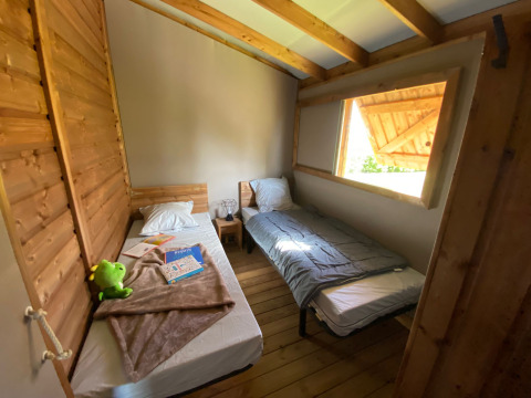 Kamer met twee eenpersoonsbedden, houten muren en groot raam in Cabane lodge Sweet Flower Premium, Frankrijk.