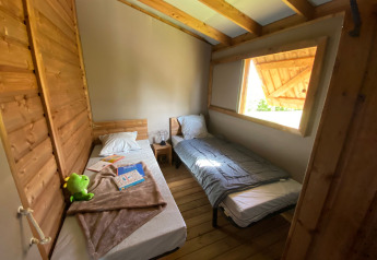 Habitación con dos camas individuales, paredes de madera y gran ventana en Cabane lodge Sweet Flower Premium, Francia.