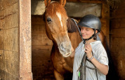 Una chica con casco de equitación junto a un caballo marrón en un establo en Feather Down Ecuries de Gapennes, Francia.