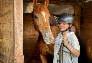 Una ragazza con casco da equitazione accanto a un cavallo marrone nella stalla di Feather Down Ecuries de Gapennes.